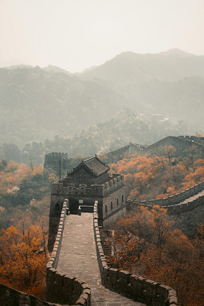 Scenic view of the Great Wall of China surrounded by autumn foliage and foggy mountains.